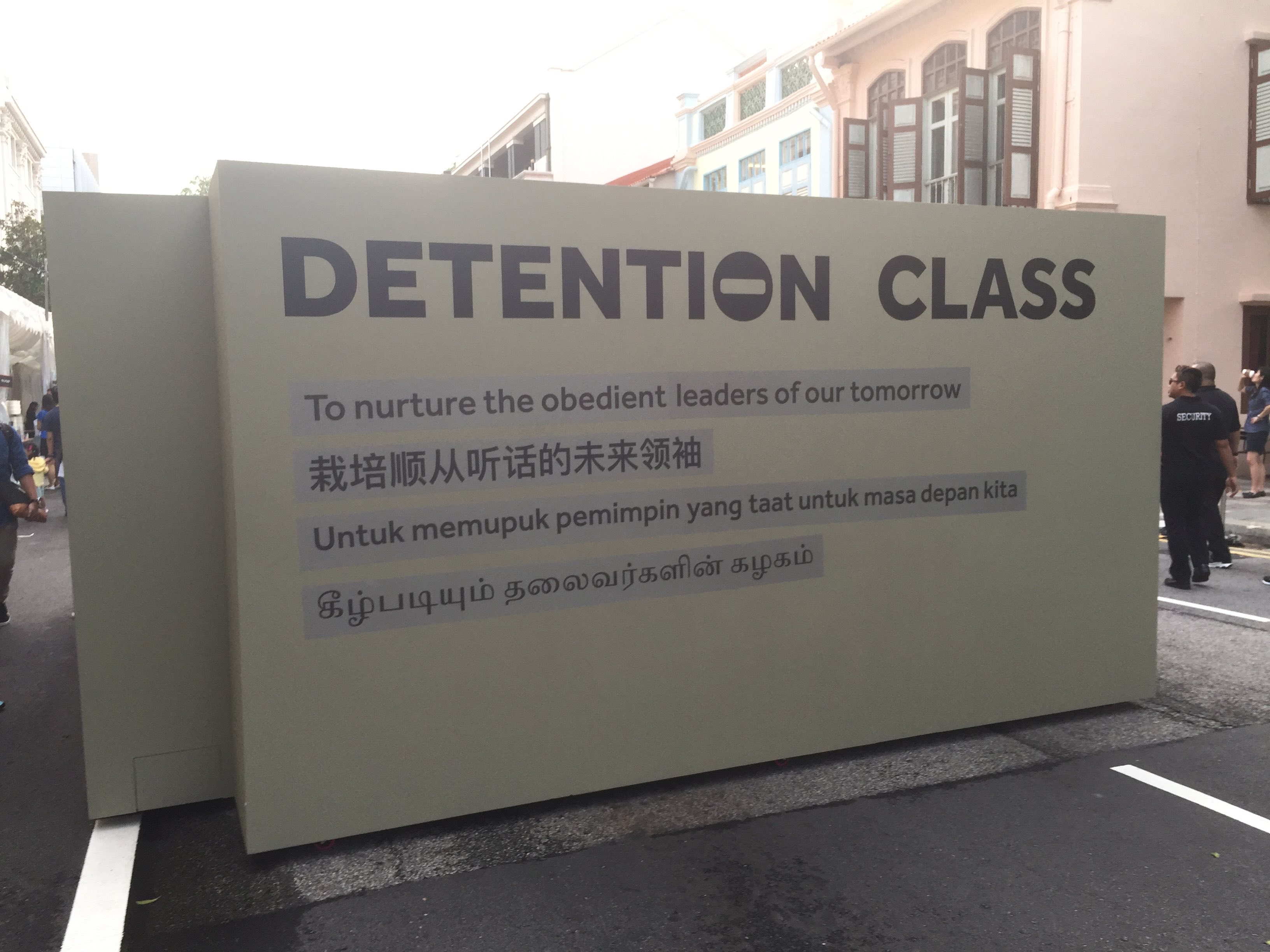 Photograph of a wall placed on road with the heading, Detention Class. Next four lines are in four different languages: english, chinese, malay, and tamil. The first line in english reads, to nurture the obedient leaders of our tomorrow.