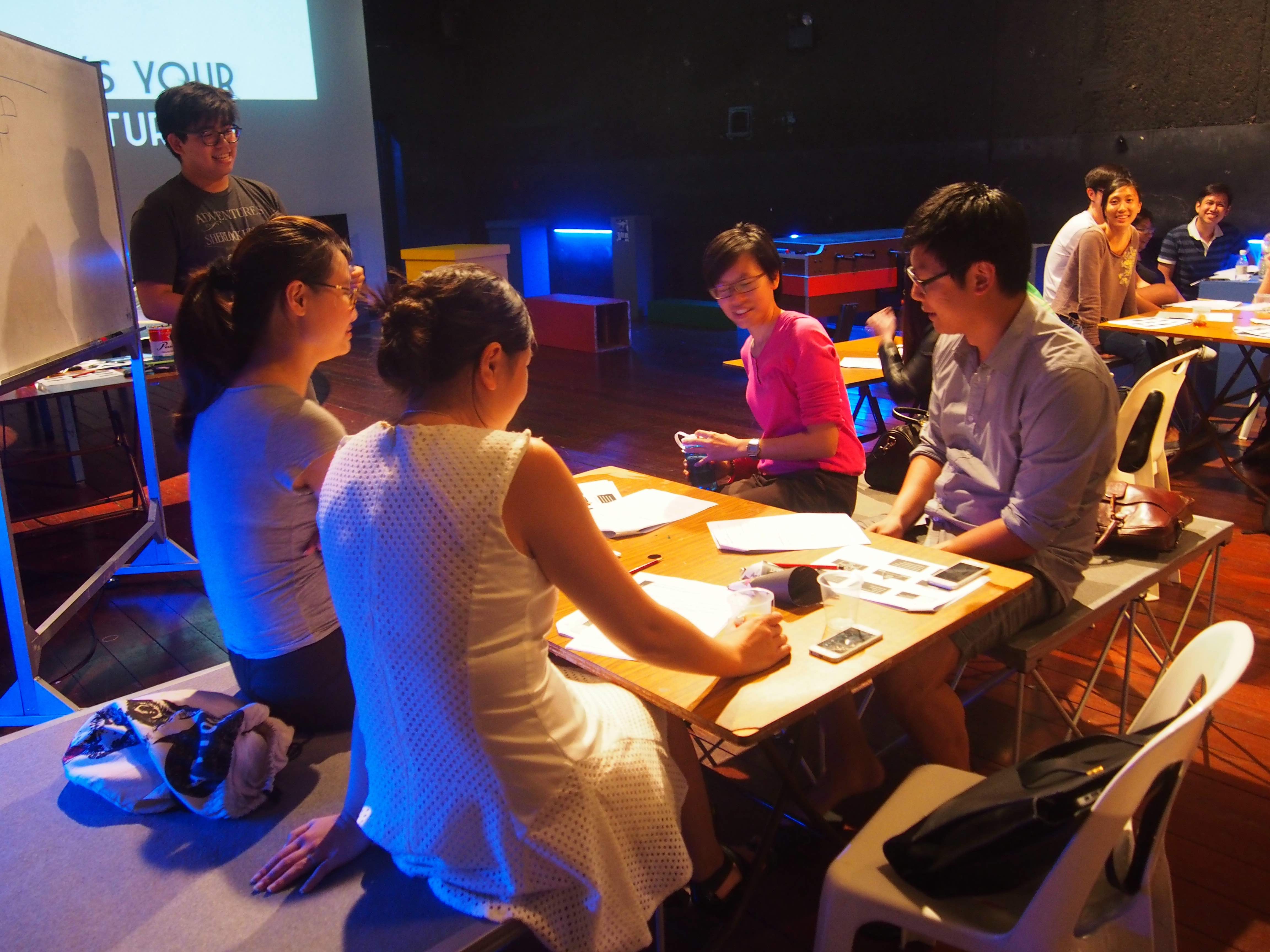 Photograph of participants at a table doing some activity as the trainer observes.