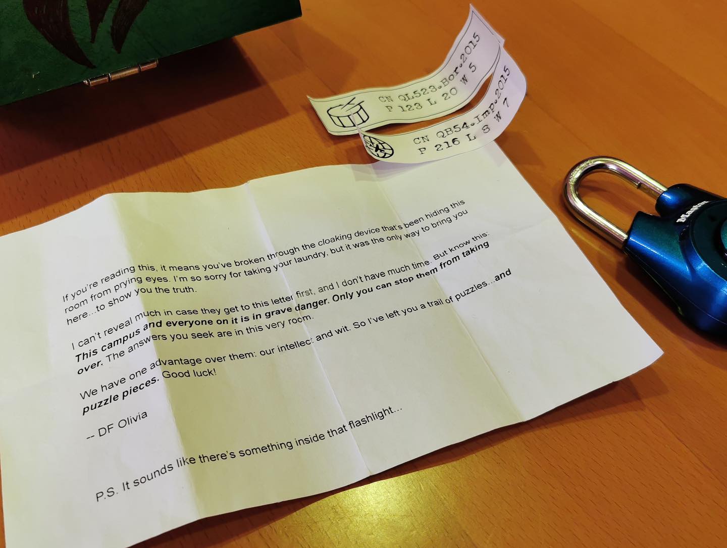 Photograph of a note, some codes on strips of paper, and a directional padlock lying on a wooden table.